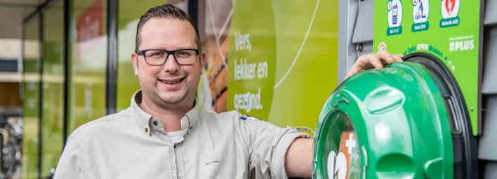 PLUS-medewerker bij een AED-kast aan de buitenkant van de winkel.