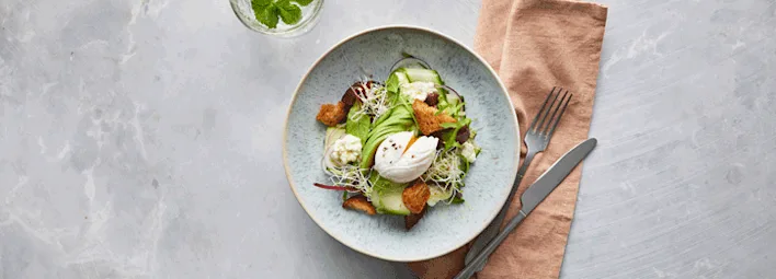Frisse salade bestaande uit groene bladeren, avocado, croutons, kiemen en een gepocheerd ei