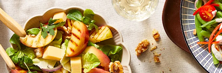 Zomerse saladerecepten van drie kleurrijke salades in kommen: één met aardbeien, feta en groene bladeren; een tweede met gegrilde perzik, walnoten en kaasblokjes; en een derde met sperziebonen, cherrytomaten en rode paprika, afgemaakt met romige dressing.