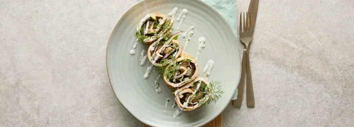 Wraps gevuld met groenten, gegarneerd met verse dille en besprenkeld met een witte dressing.