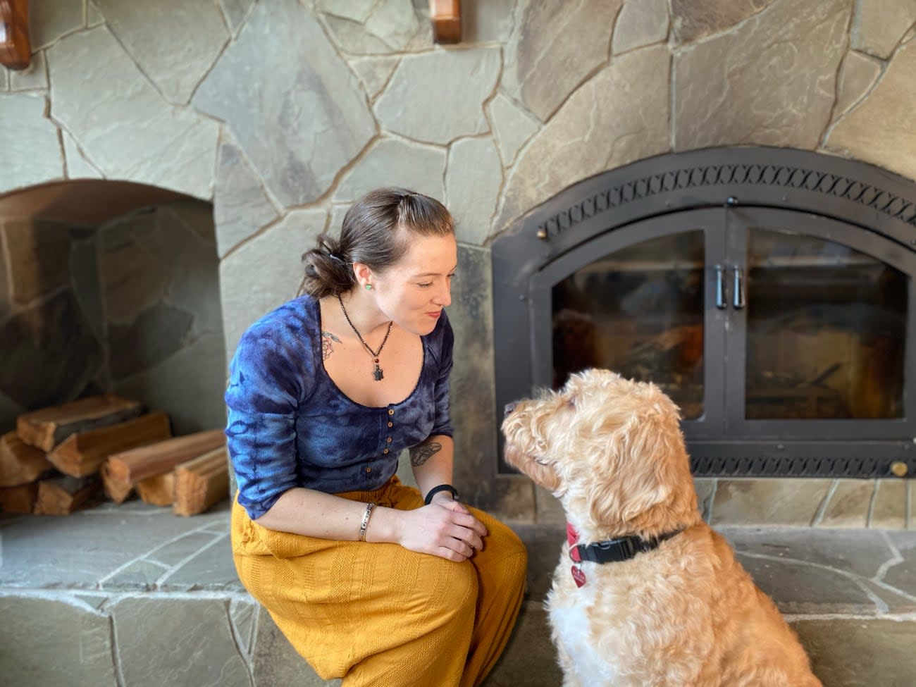 Photo of Marcy Sutton with her dog next to a fireplace.