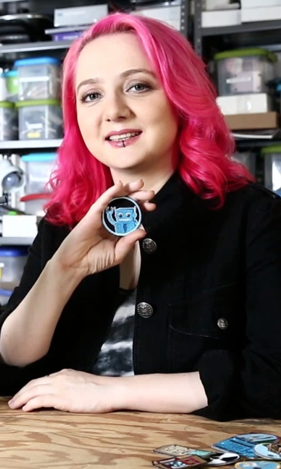 Portrait photo of Limor Fried holding a cute robot badge.