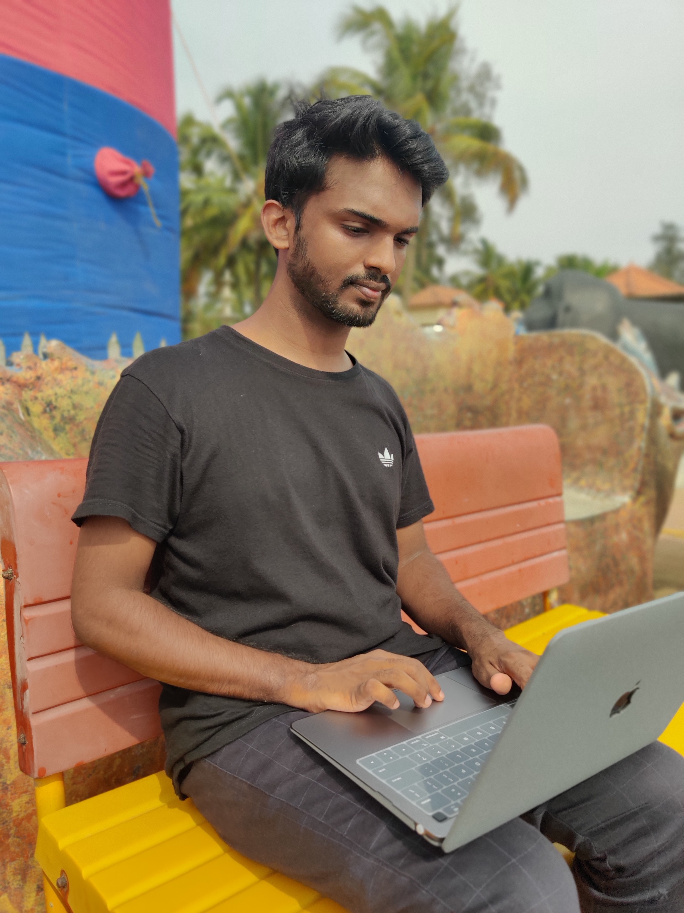 Author Liyas sitting on a colorful outdoor bench working on his laptop