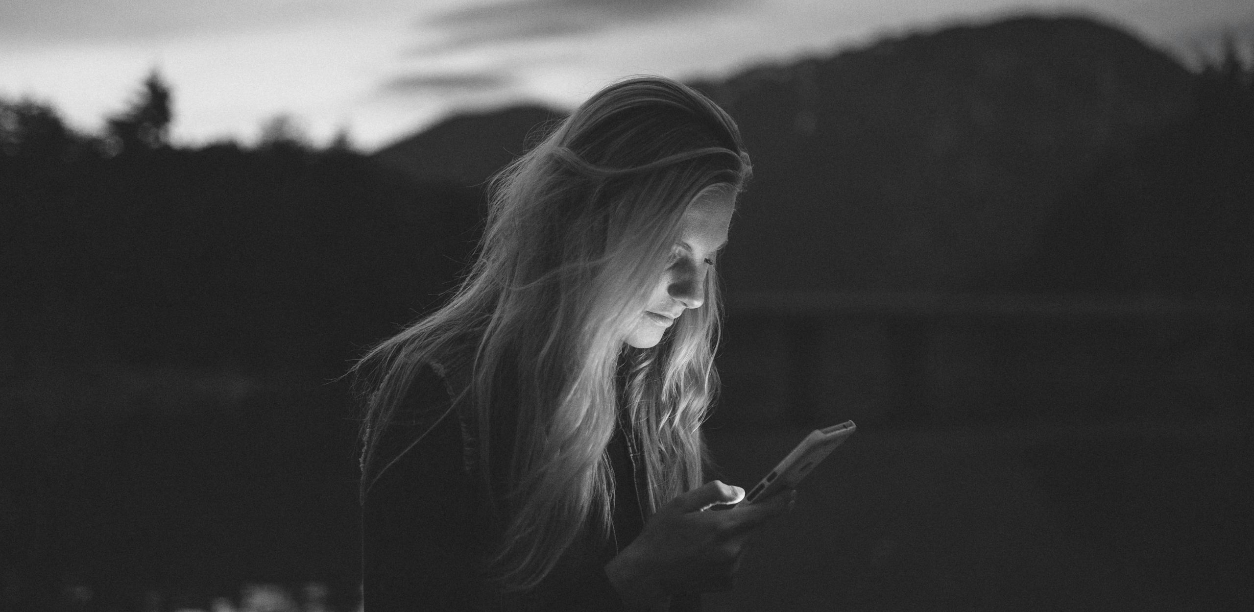 A woman peers into a glowing smartphone, contemplating the tech industry. by Becca Tapert