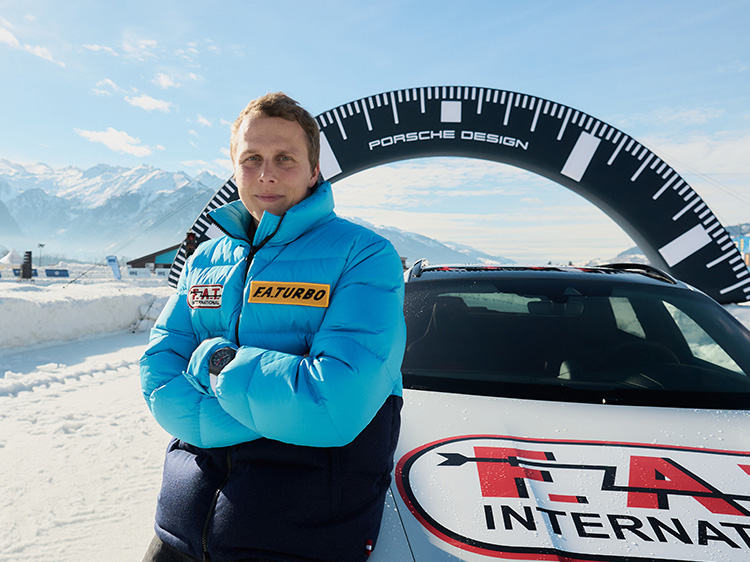 Man crossed arms leaning on Porsche in snow, mountain backdrop