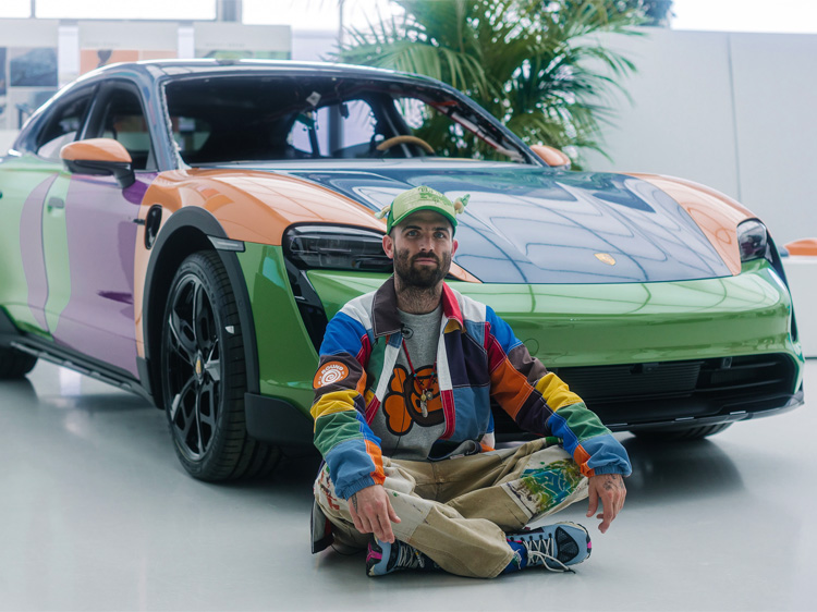 Man in multicoloured jacket sits in front of multicoloured Porsche