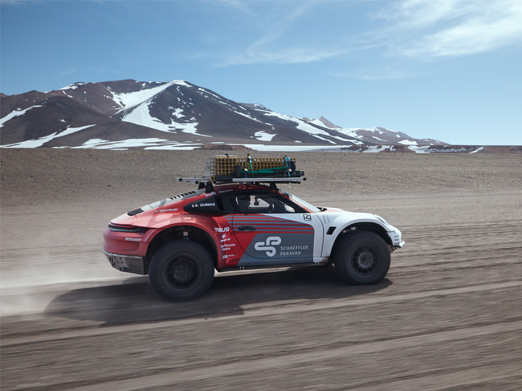 Off-road Porsche 911 driving along rocky terrain, snow-capped volcano behind