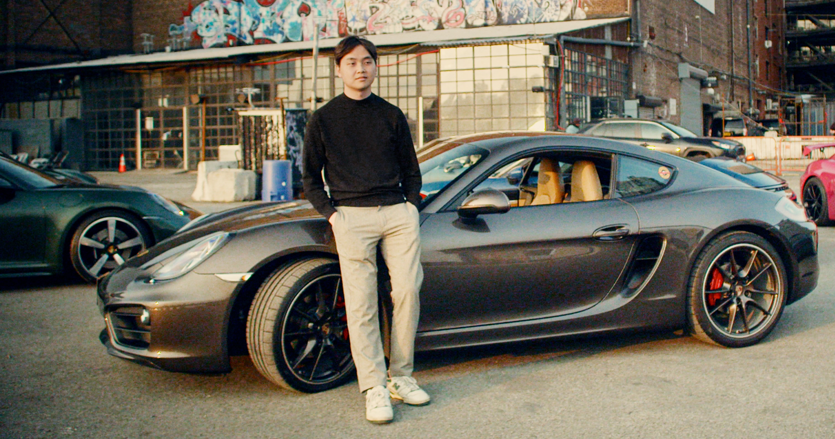 Man in chinos stands next to brown Porsche Cayman