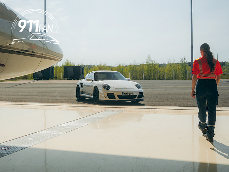 Woman walking towards white Porsche 911 with aeroplane in hangar
