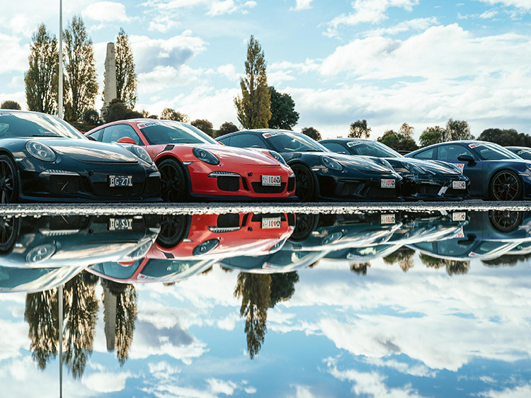Five Porsche cars in a line reflected in water