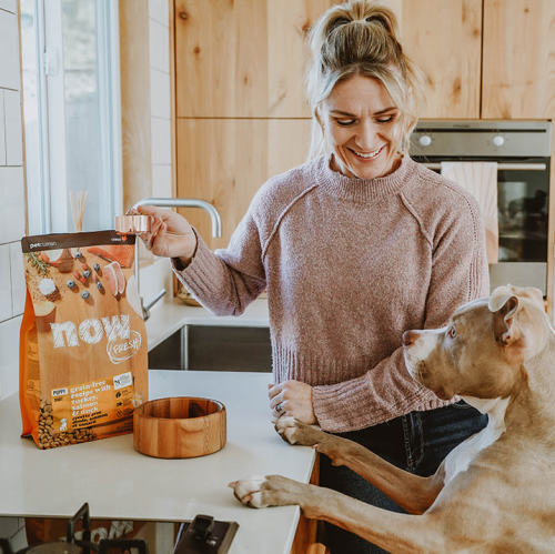Woman in kitchen with dog with paws on counter and bag of NOW FRESH kibble