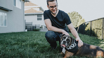 GO-SOLUTIONS-brown-dog-with-go-bandana-laying-on-green-grass-with-pet-parent