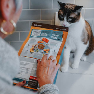 Woman reading ingredients on cat food bag in front of cat