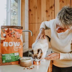 Senior woman petting Snowshoe cat on counter with NOW FRESH kibble bag
