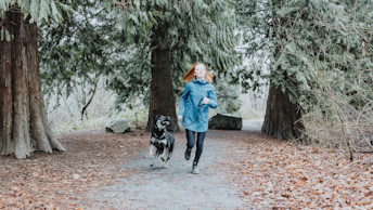Black dog running with pet parent outside in leafy area