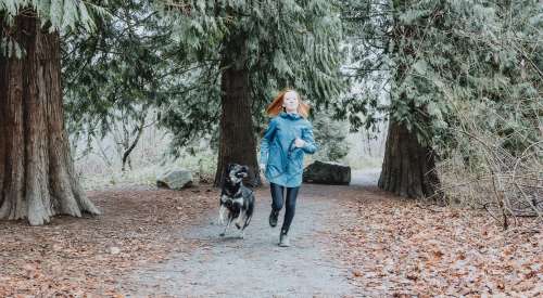 Black dog running with pet parent outside in leafy area