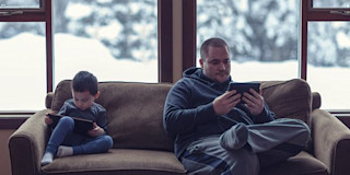 A man and a boy reading on tablets
