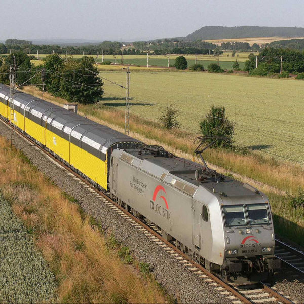 Das Bild zeigt eine Lok mit Autowaggons. Neben den Gleisen sieht man grüne Felder. Viele Züge sind für den Güterverkehr unterwegs und transportieren Waren. 
Copyright: TX Logistik AG/ Netzwerk Europäischer Eisenbahnen (NEE)