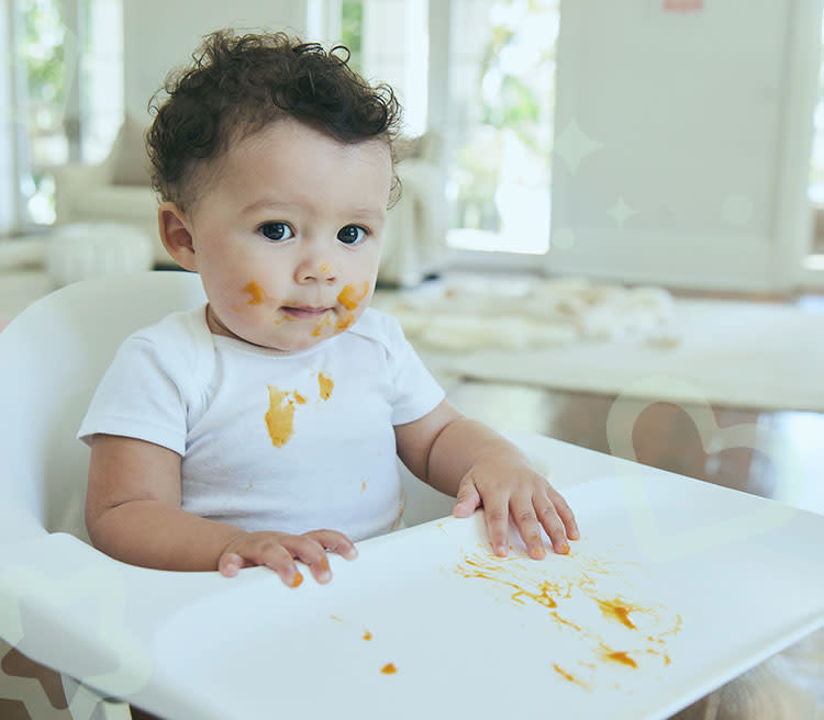 A little child sitting in a baby chair covered by carrot stains