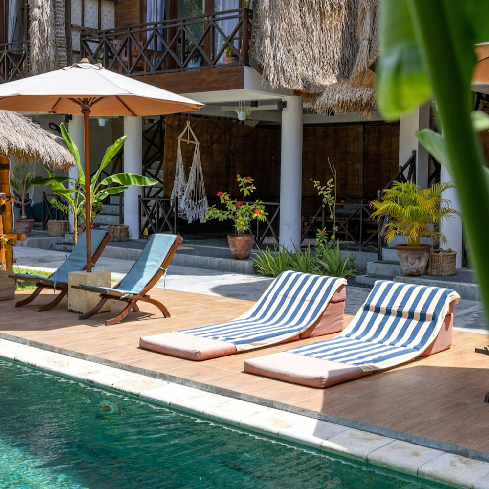 Lounge chairs by a poolside outside of a thatched roof resort