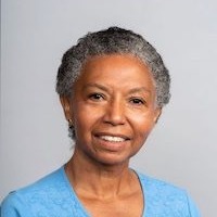 Headshot of a short-haired black woman smiling broadly against a plain backdrop.}}