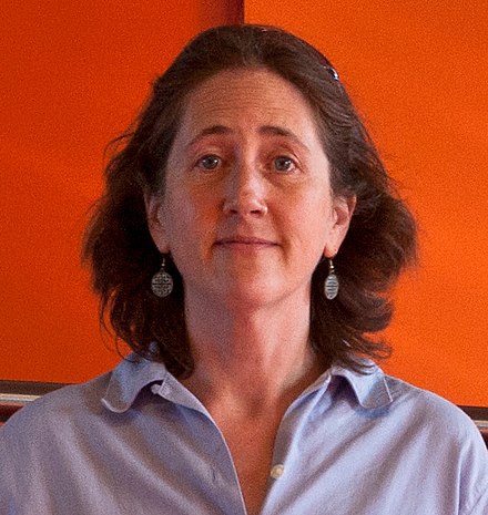 headshot of a woman against an orange background looking straight at the camera}}