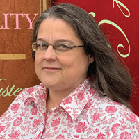 Headshot of a white woman with classes in a floral shirt.}}