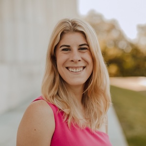 Informal headshot of a young white woman in front of a lawn and a building with pillars.}}