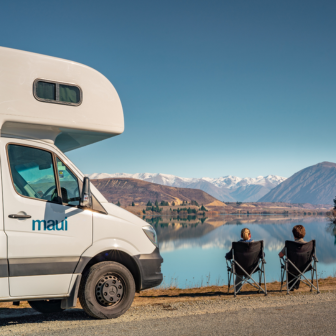 Caravana con dos personas delante de un lago