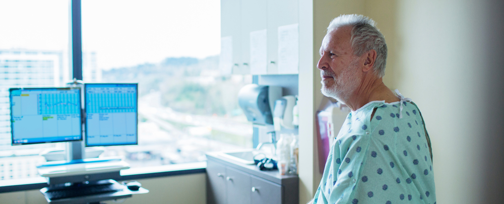 man with gray hair wearing hospital gown sitting in hospital room