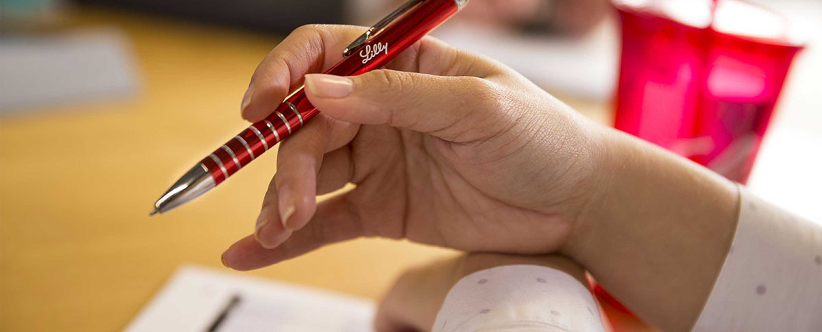 close up of a hand holding a Lilly branded red pen