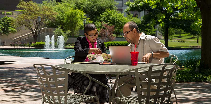 two people working at table outside in front of fountain