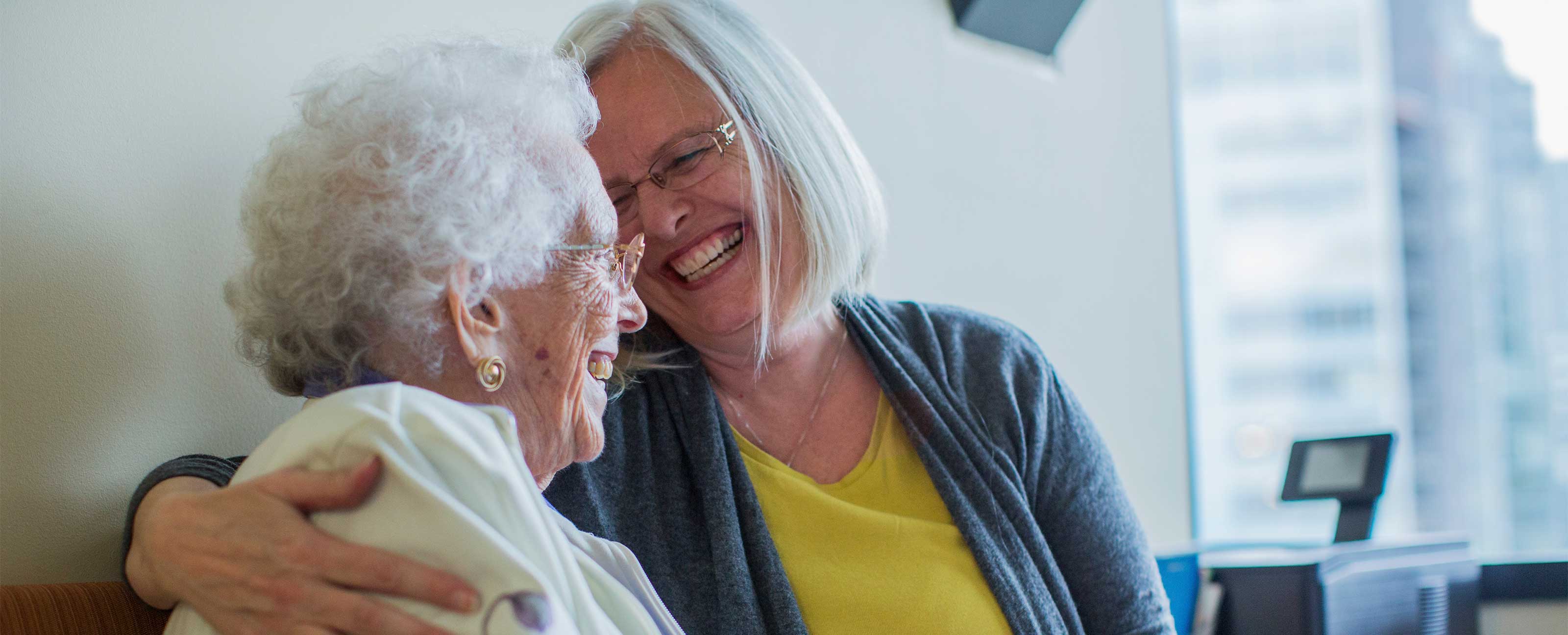 elderly mother and daughter hugging and laughing