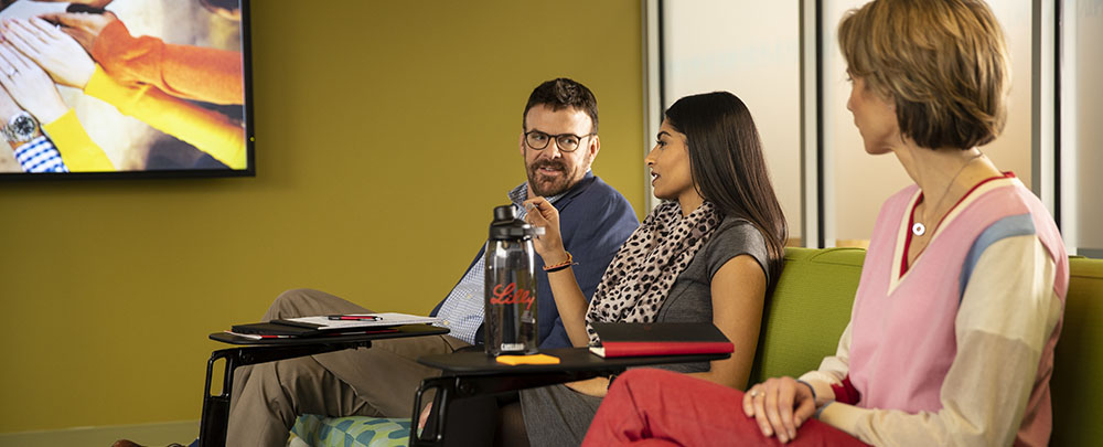 Three employees sitting on couch at work, talking