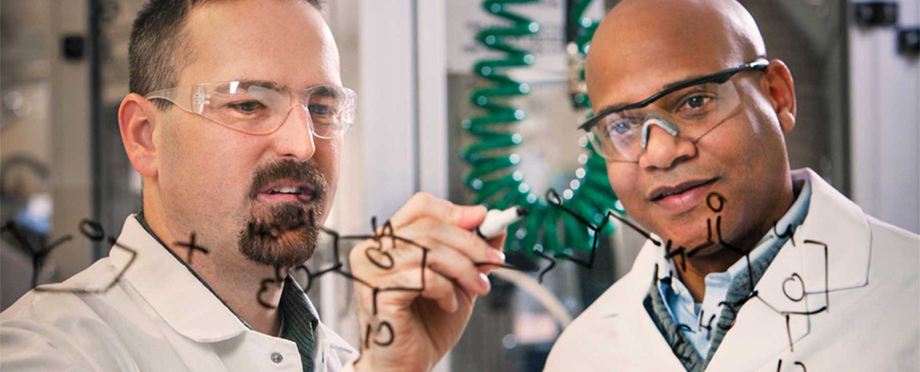 two scientists writing on glass board