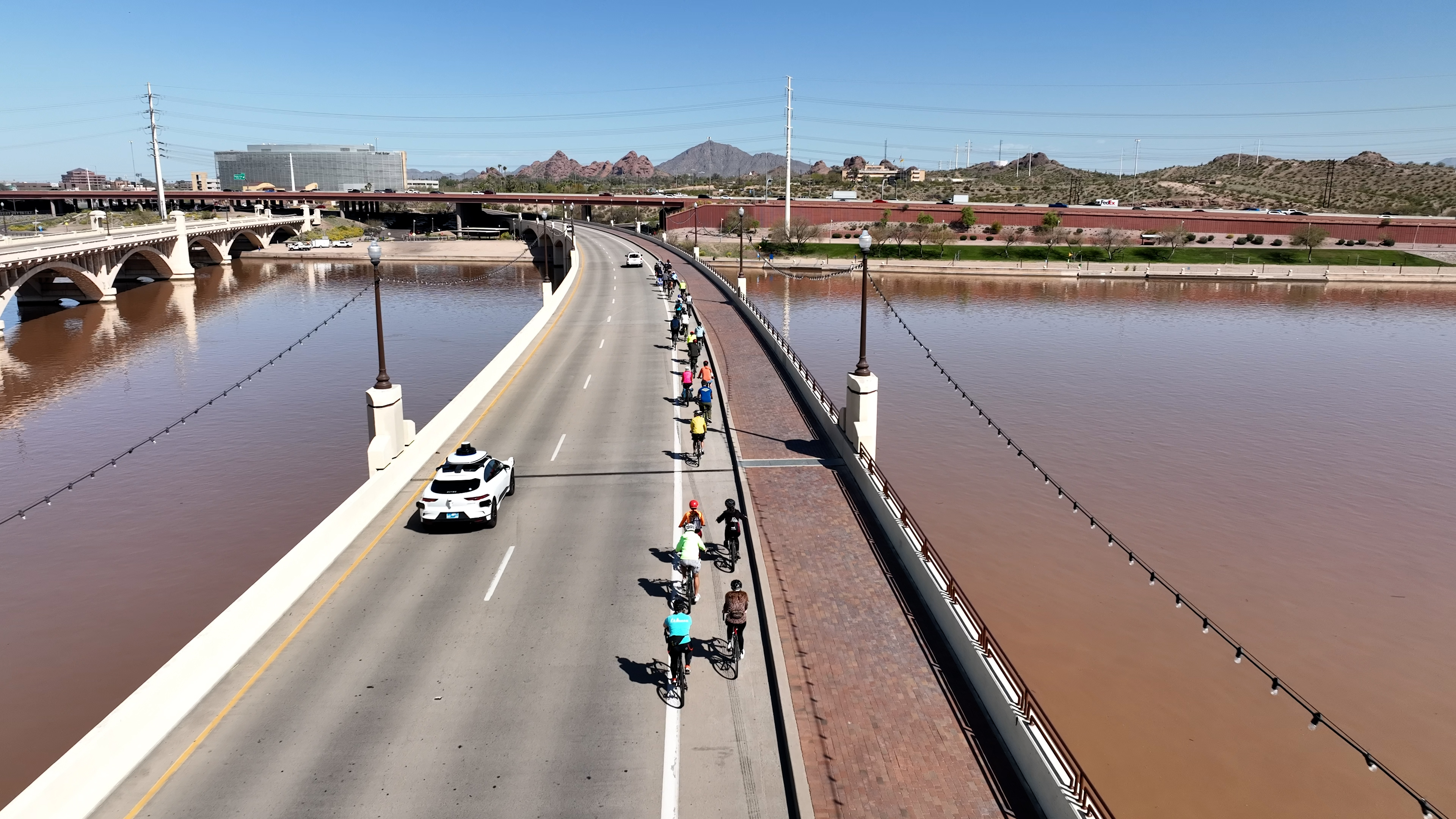 Waymo vehicle in far left lane crossing a bridge alongside many cyclists in the bike lane on the far right
