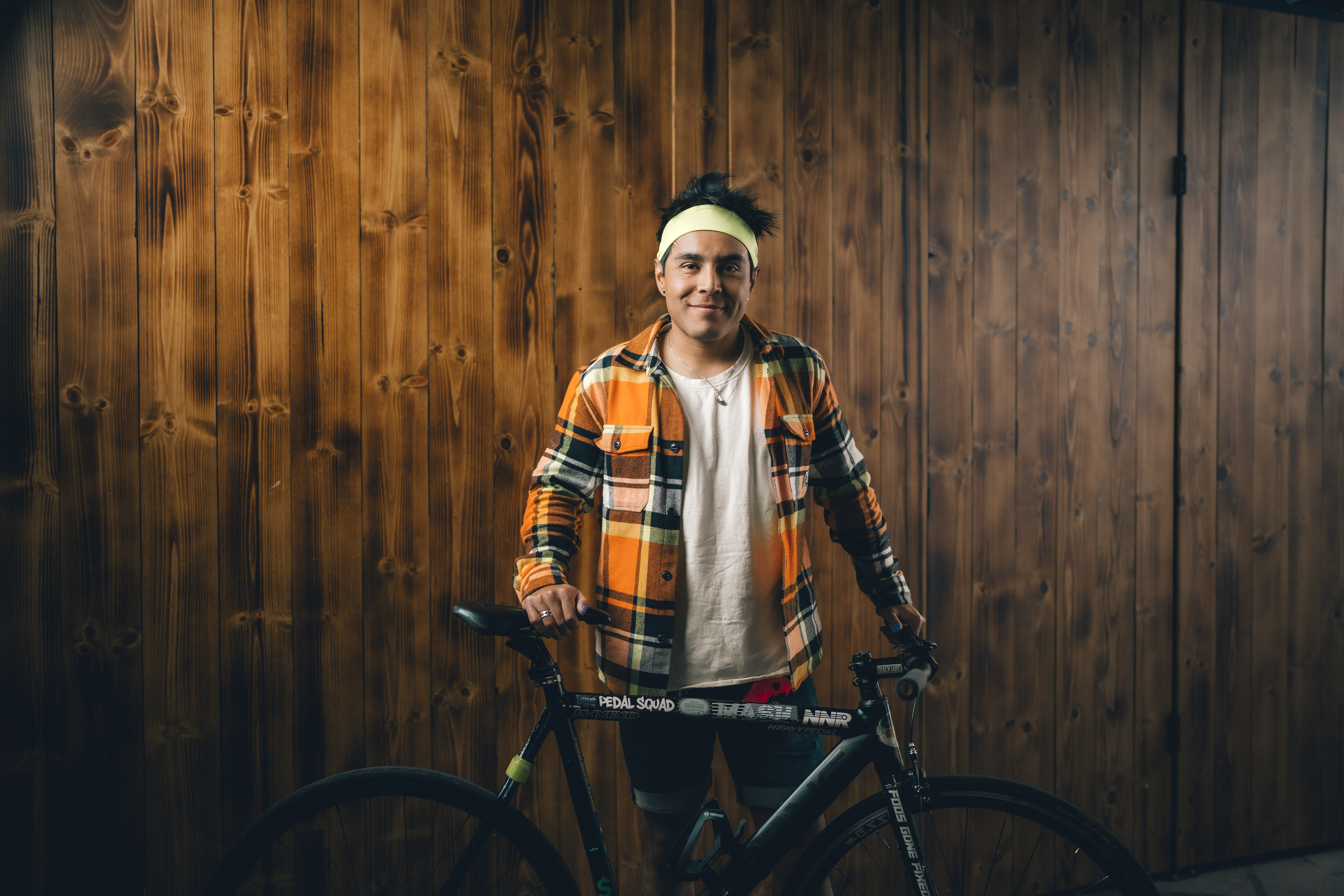 Becket standing in front of a wood paneled wall holding his bike, smiling at the camera