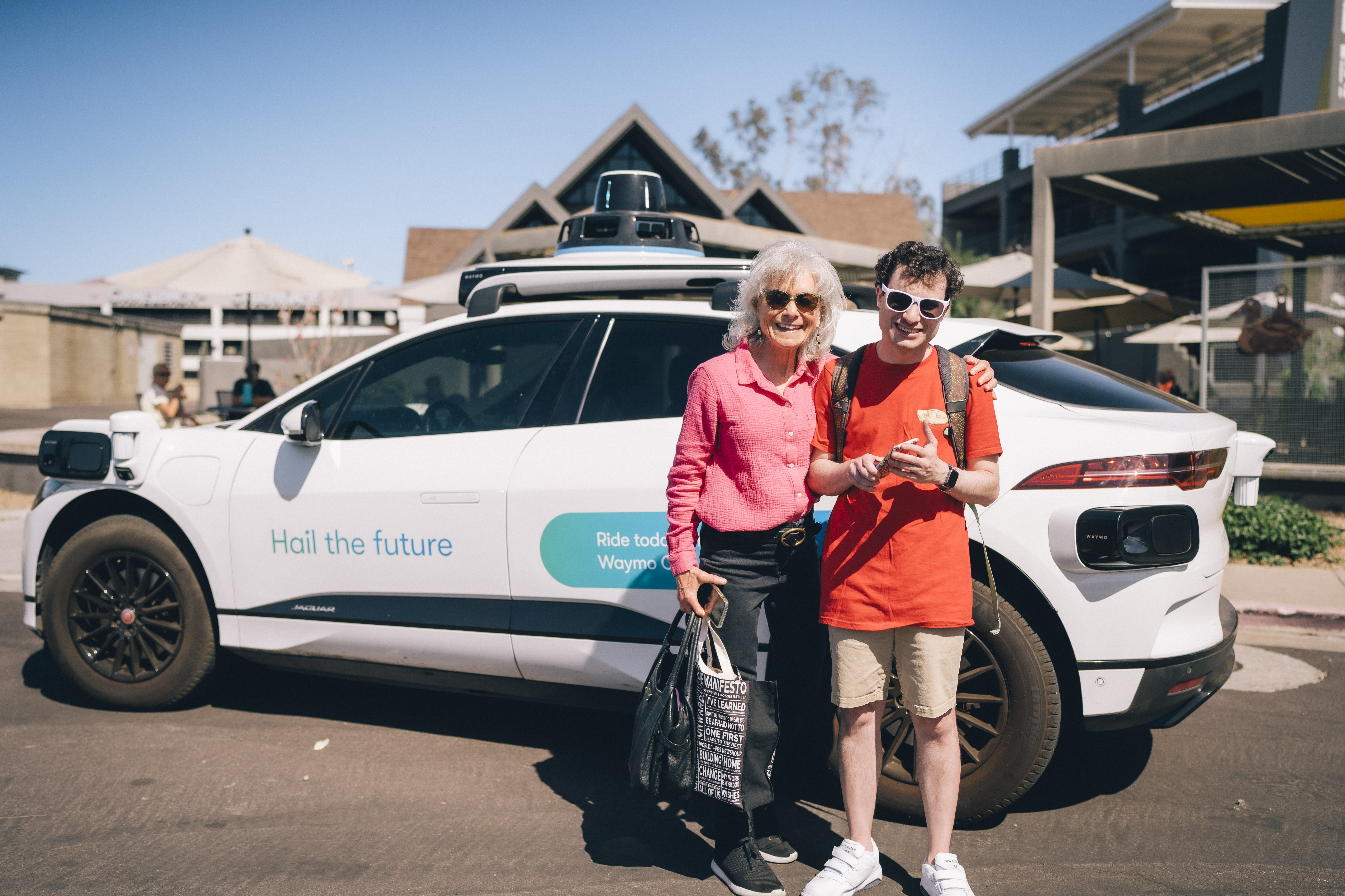 Denise and Matt Resnik standing next to a Waymo autonomous vehicle, in front of Duck and Decanter