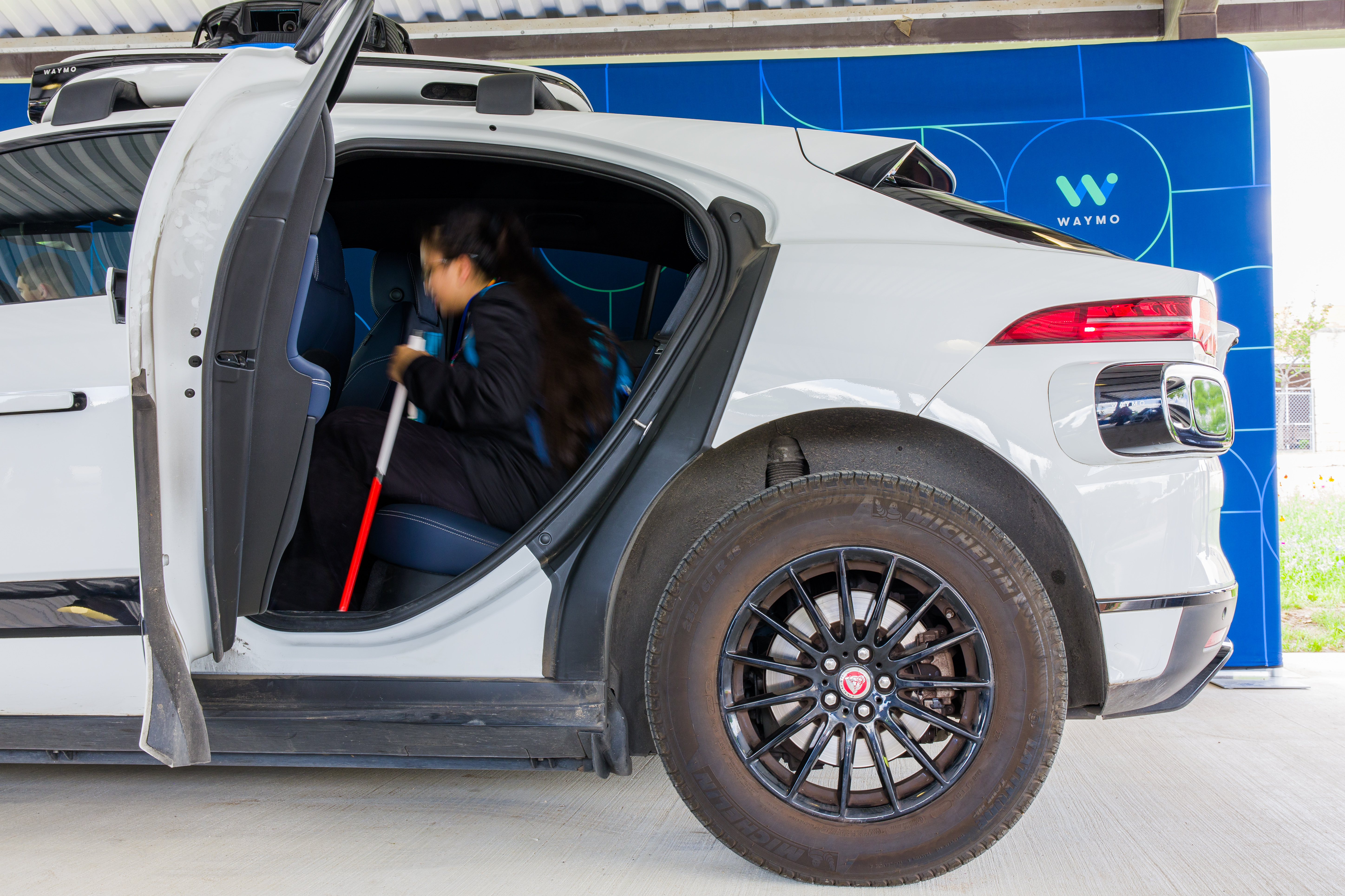 Young girl with a cane sitting in the backseat of a Waymo vehicle with the door open
