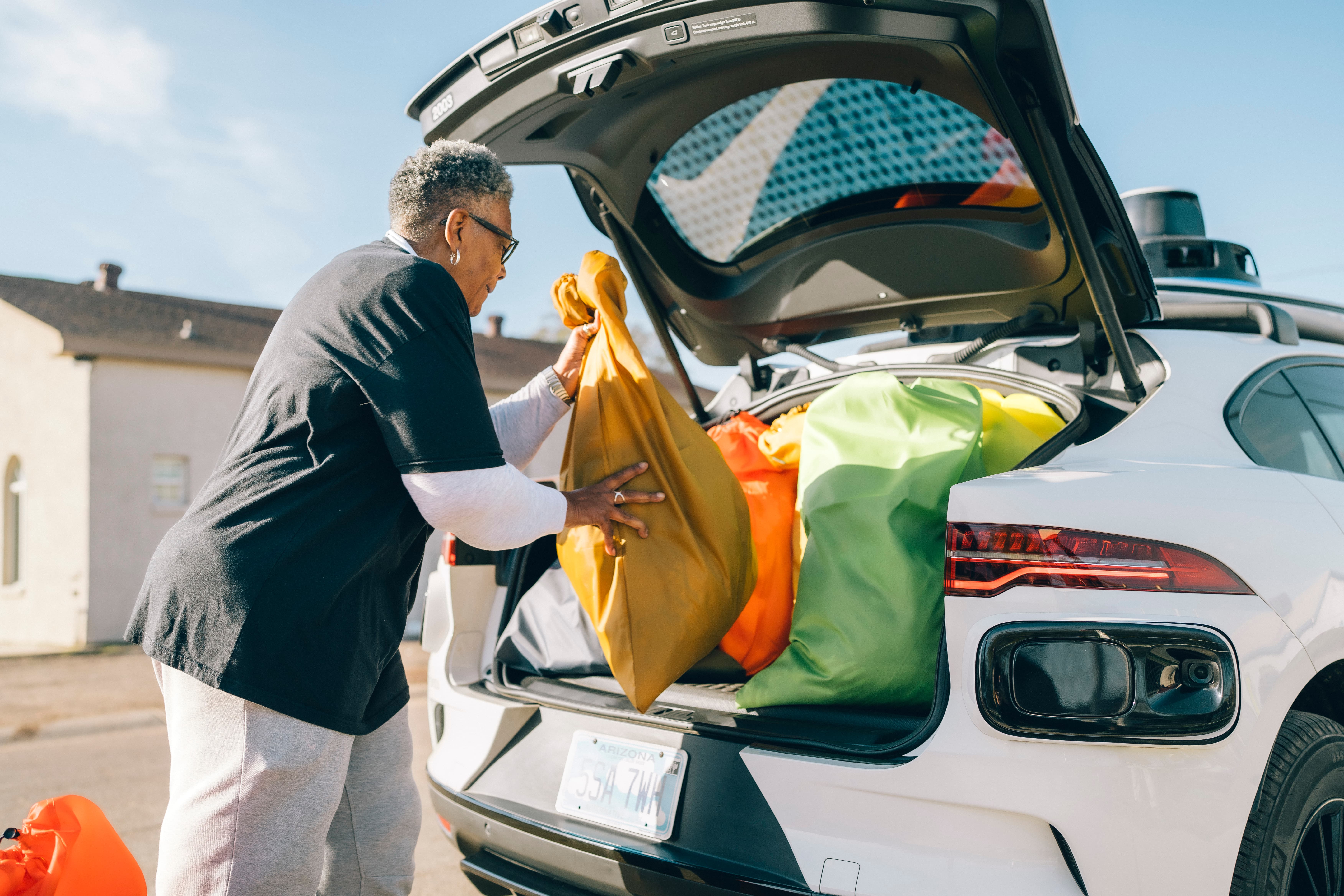 Woman loading bags of laundry into the trunk of a Waymo vehicle