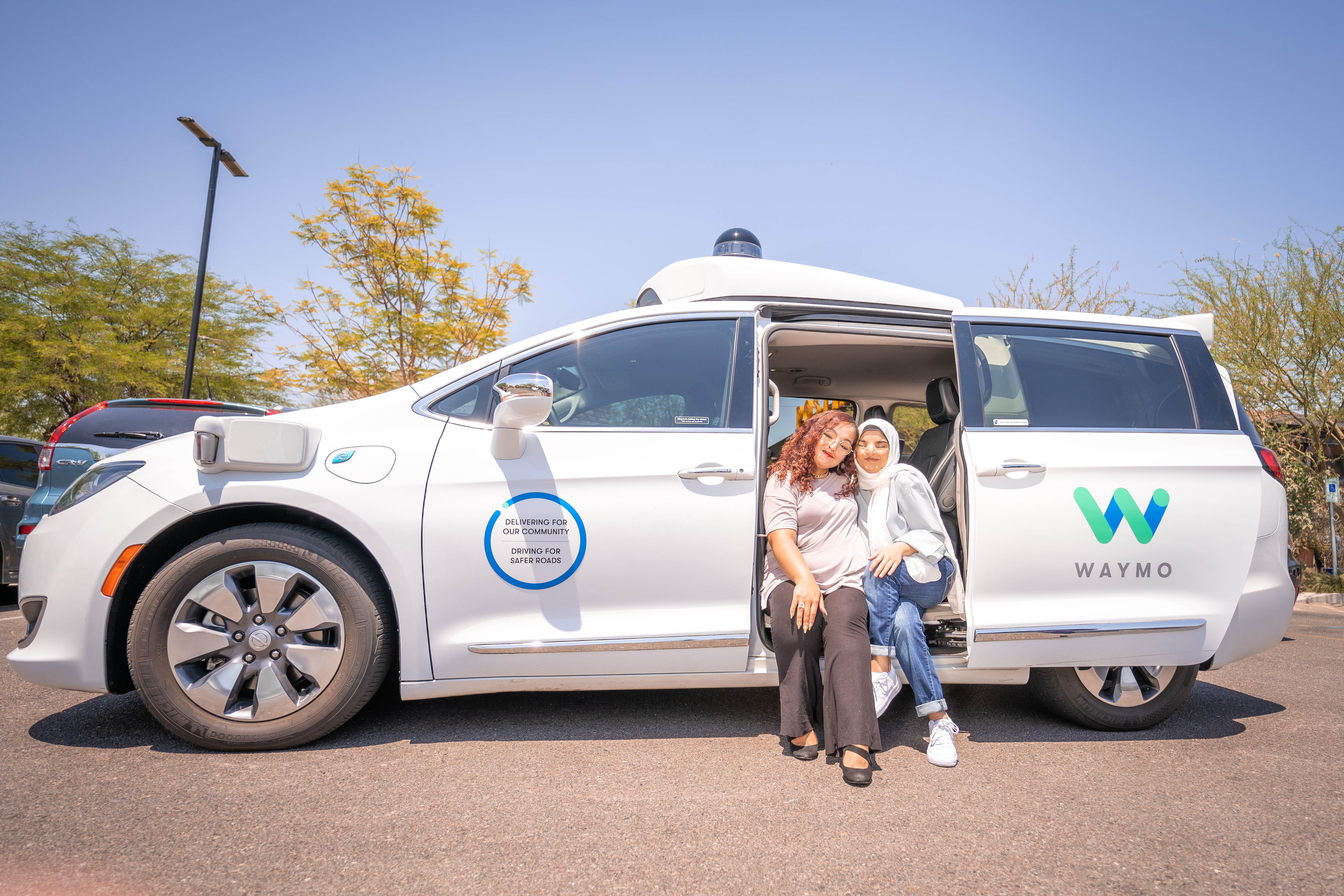 Two people sitting in the doorway of a Waymo autonomous vehicle