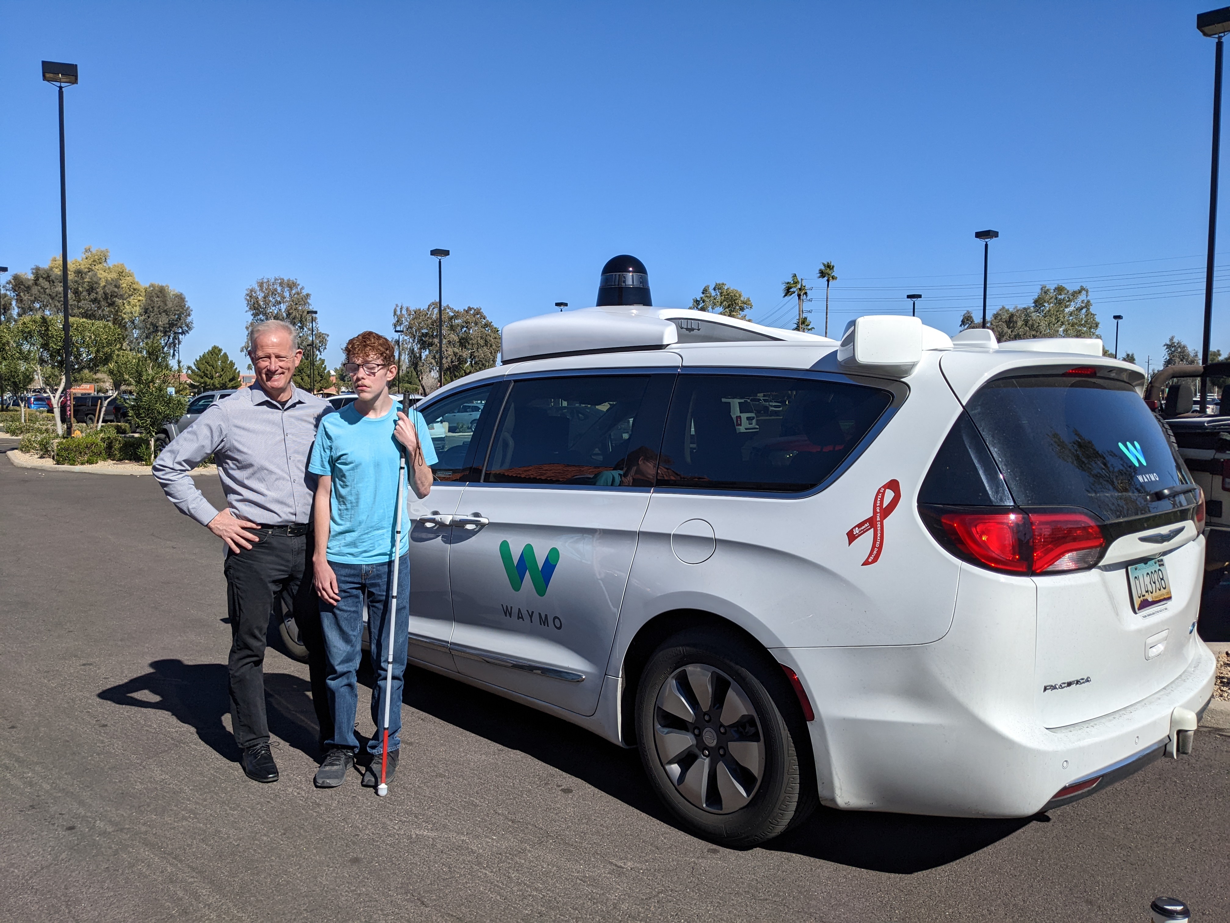 Man and woman, Marc Ashton and Ethan Roberts, standing in front of Waymo autonomous vehicle