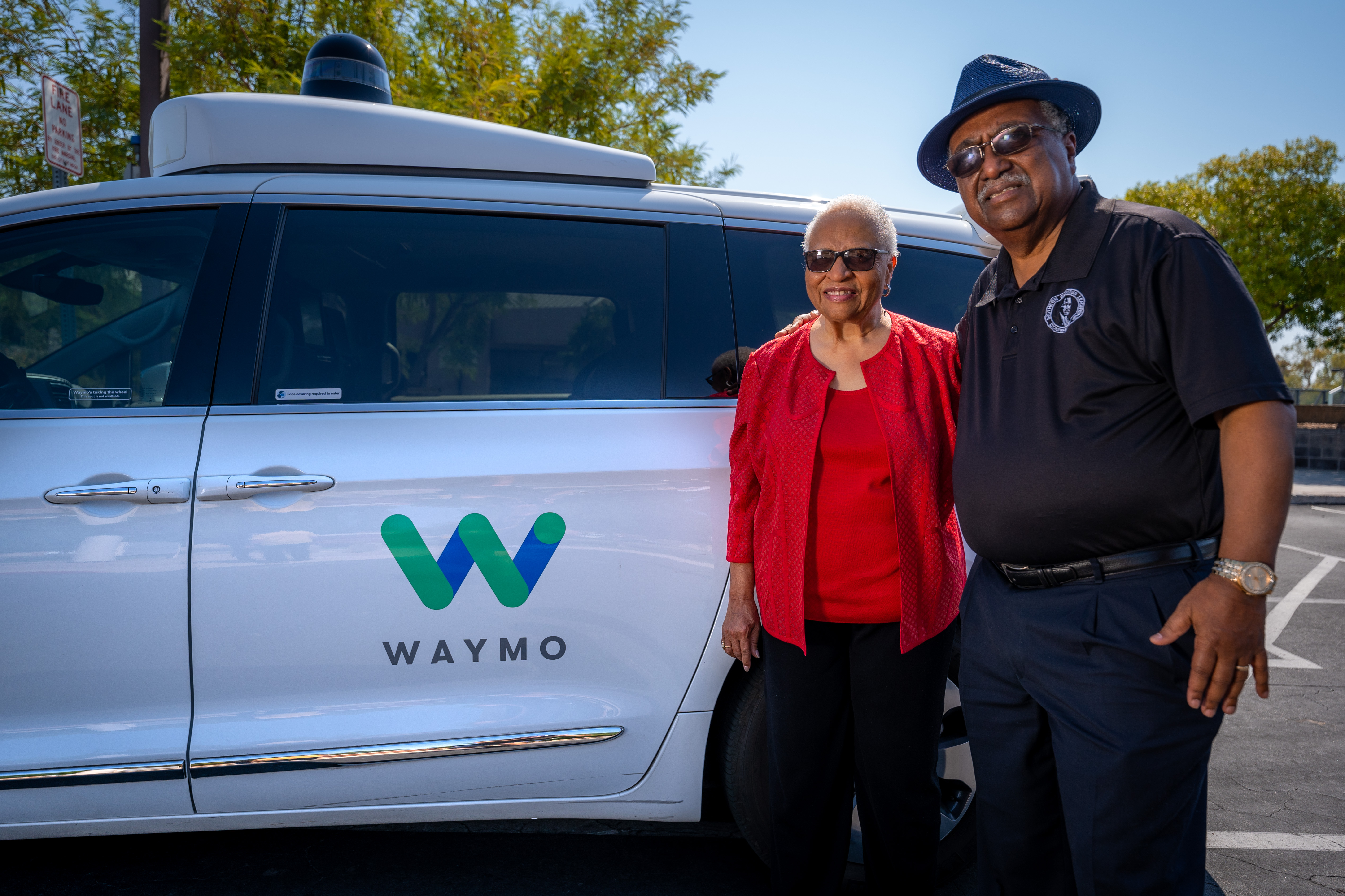 Woman and man standing in front of Waymo autonomous vehicle