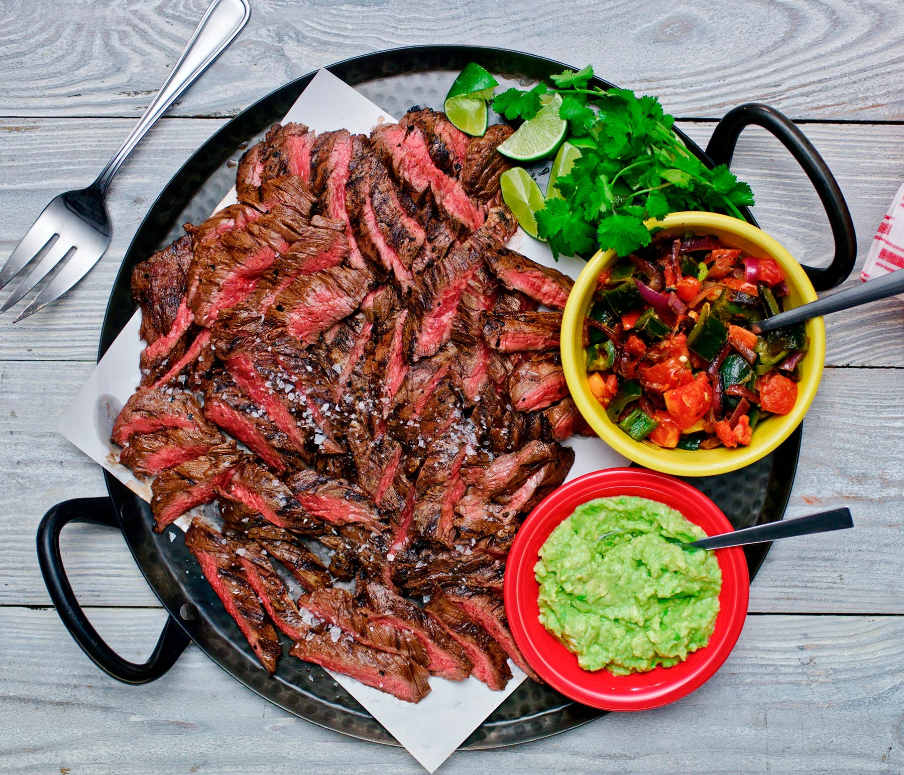 Overhead shot of cerveza beef fajita on a cast iron platter with sides of guacamole and salsa