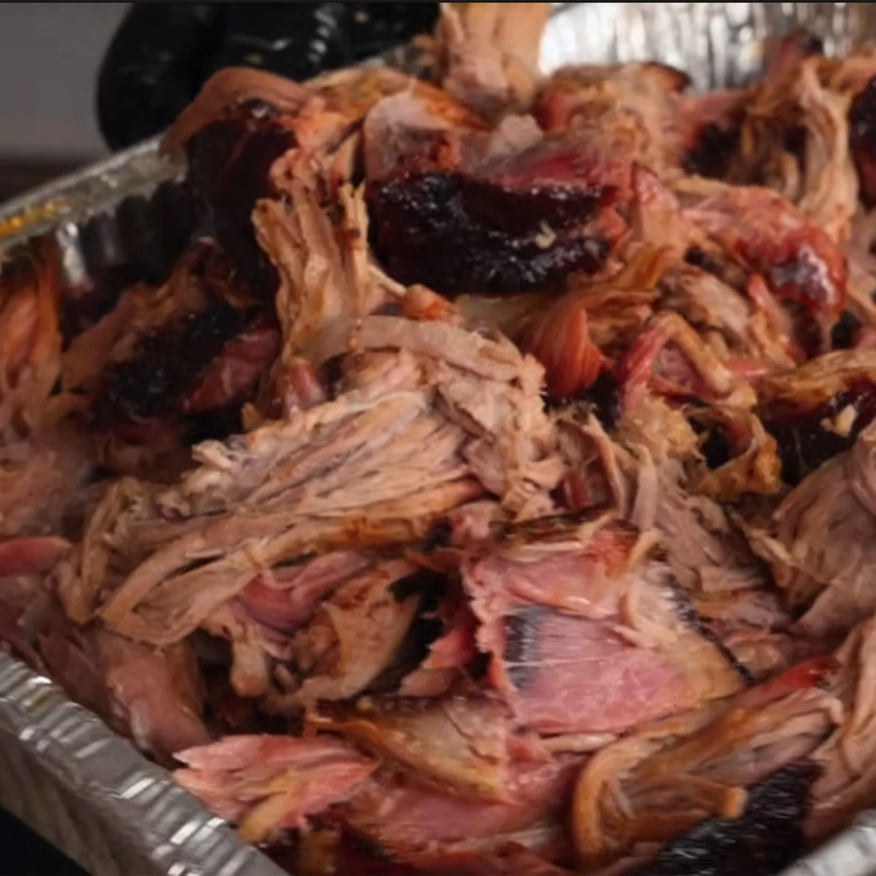 Tender pulled pork stacked high inside a disposable aluminum foil pan