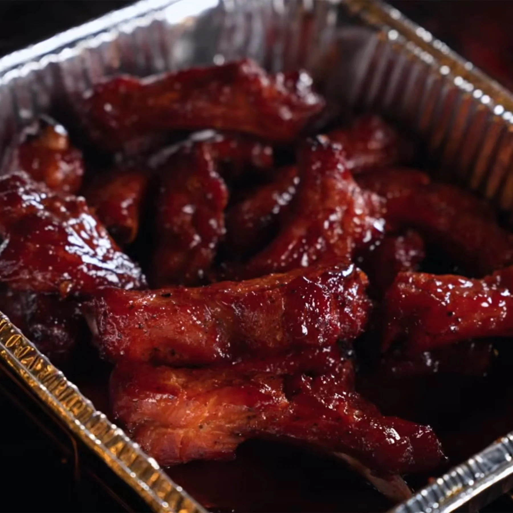Saucy barbecue ribs piled inside a disposable aluminum foil pan.