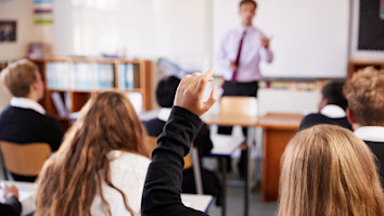 Student raising hand to ask question to teacher in classroom