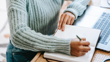 Girl writing in her notebook while using UCAS Extra on her laptop