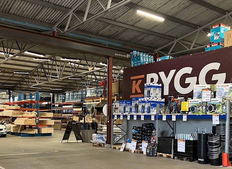 Interiör av hårdvarubutik med staplade träplankor, blåvita verktygslådor och rödbrun BYGG-skylt