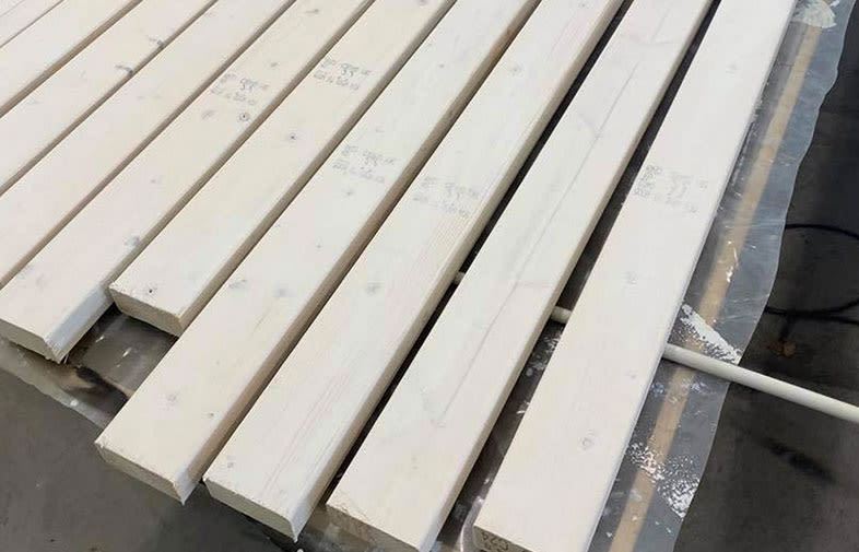 Vita träplankor ligger på plastduk på verkstadsgolvet för målning.